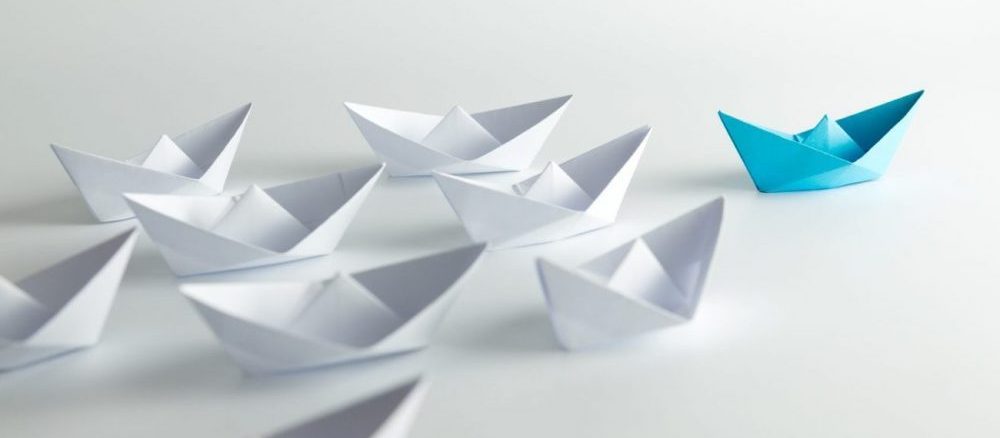 Leadership concept with blue paper ship leading among white